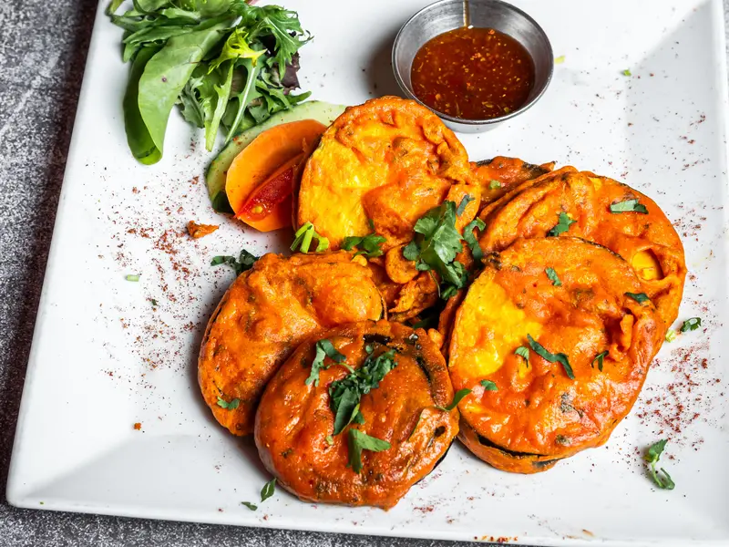 Een bord met krokante aubergine pakora, met sla en een kommetje saus