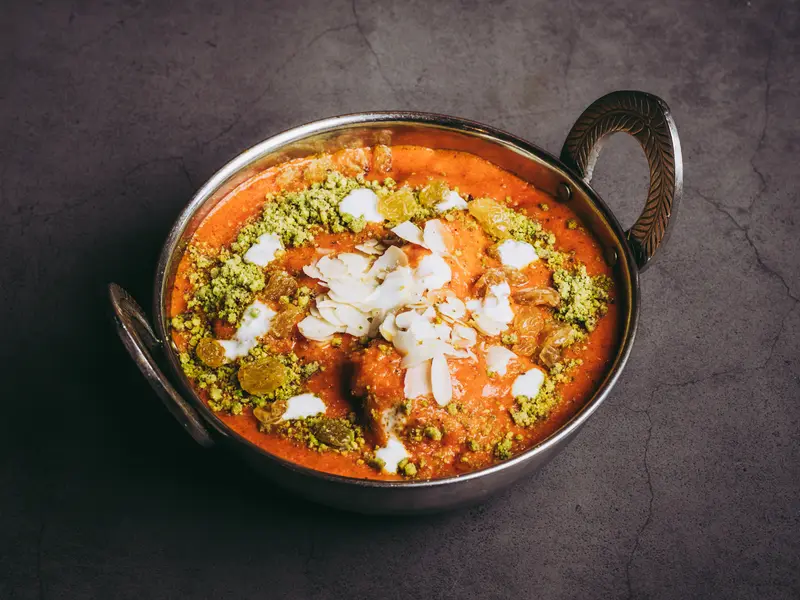 Een karahi met butter curry, bestrooid met cashewnoten, op een donkere leistenen tafel