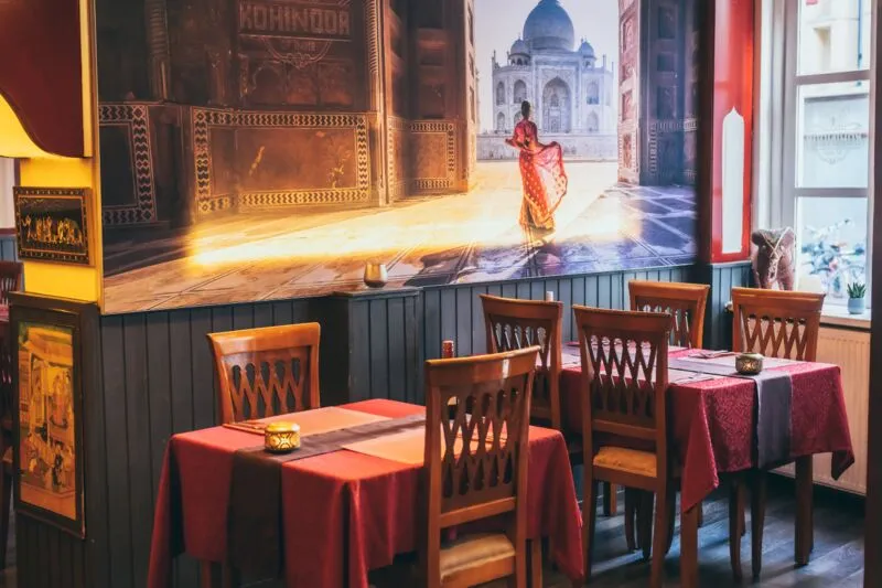Het restaurant van binnen met een grote wandschildering van de Taj Mahal en tafels met rode kleden