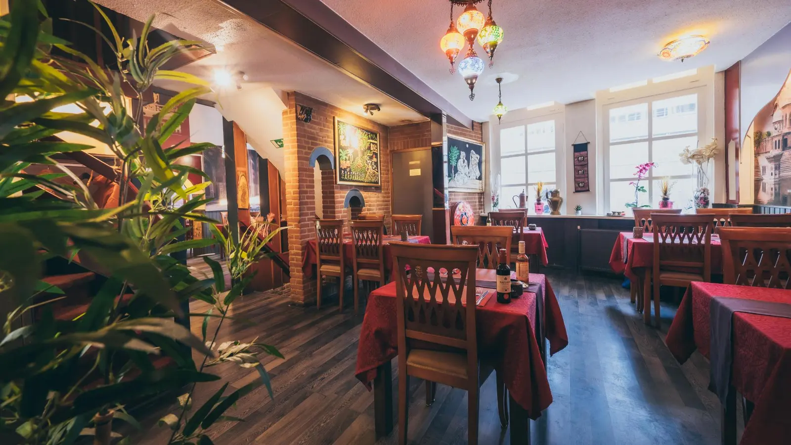 Het restaurant van binnen: houten stoelen, tafels met rode kleden, planten en warme verlichting