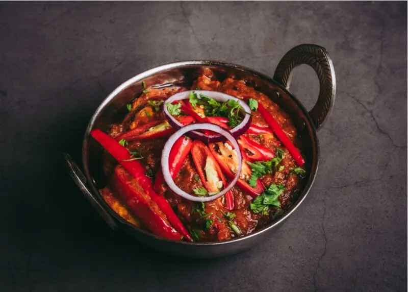 Een karahi met rode curry en ui