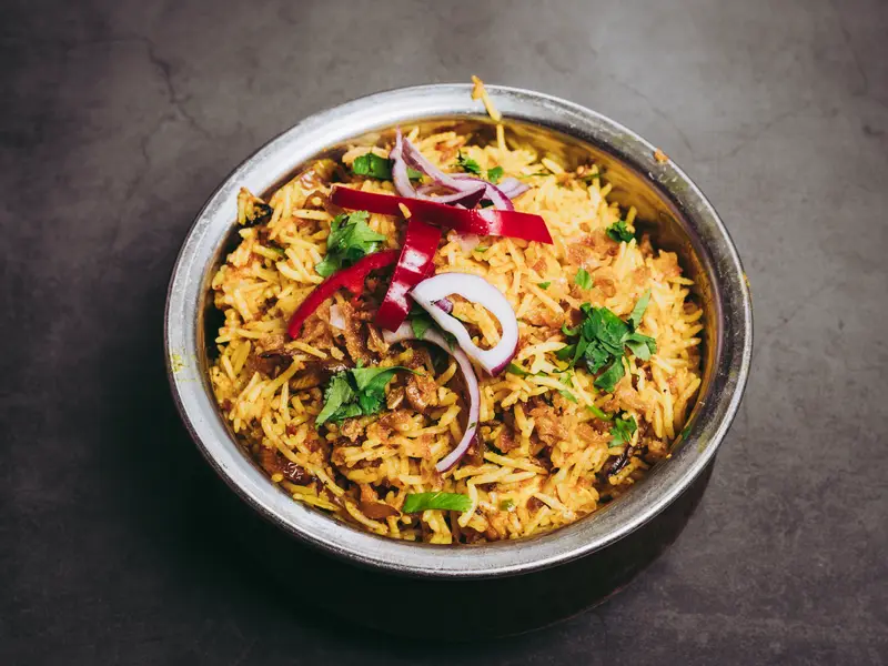 Een kom kip biryani met saffraanrijst, rode peper en ui