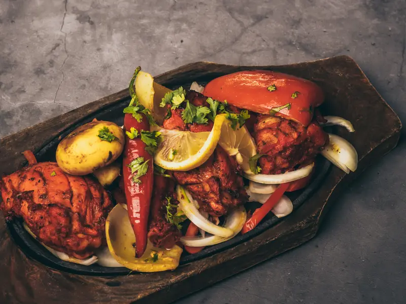 Malse tandoori kip met aardappel, citroen en rode peper op een houten plank