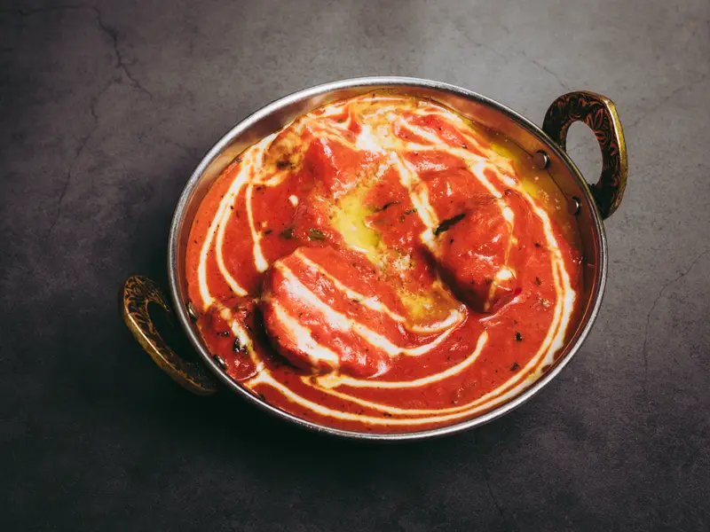 Een karahi met tikka masala in een rode saus met een wervel van room
